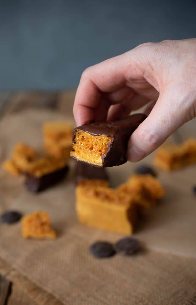 Holding a piece of 3 Ingredient Cinder Honeycomb Toffee coated in chocolate