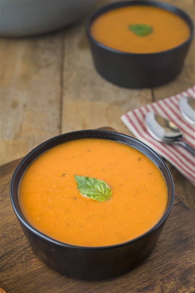 30 minute tomato basil soup in a black bowl garnished with a fresh basil leaf