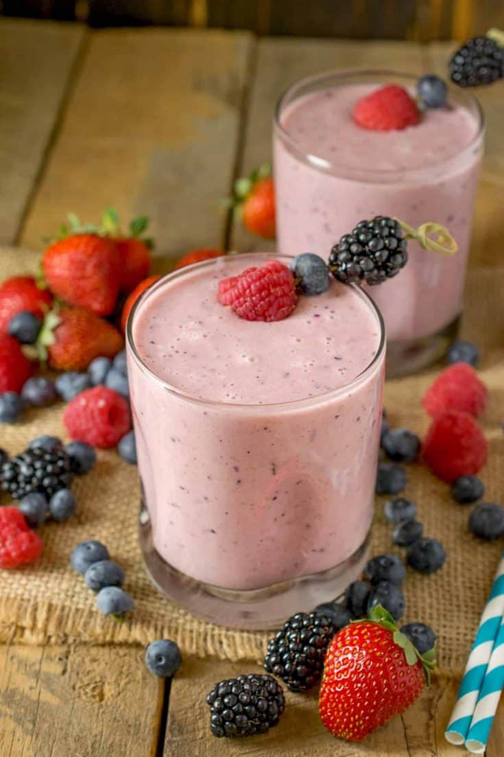 2 glasses of a berry healthy smoothie surrounded by berries
