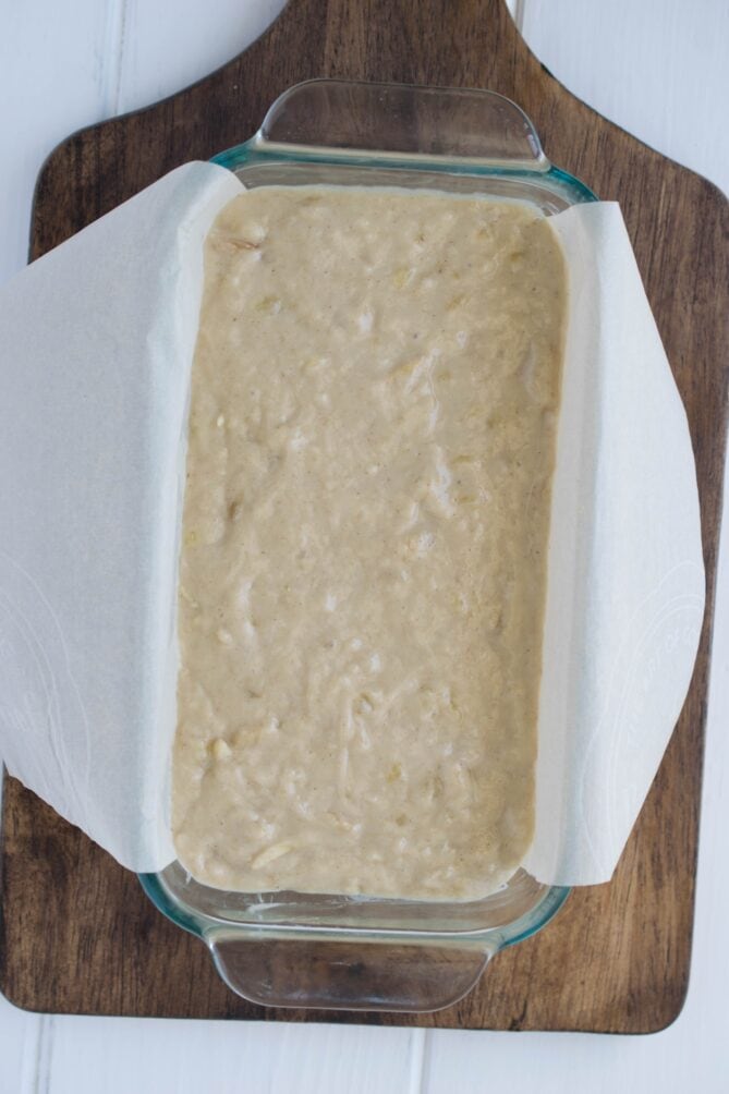 Banana bread batter in a glass loaf pan lined with parchment paper