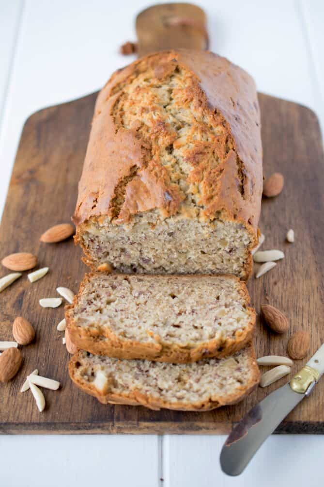 Banana bread sliced viewed from the front on a board with almonds