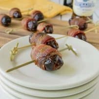 Apple stuffed bacon wrapped dates on white plates with more in background