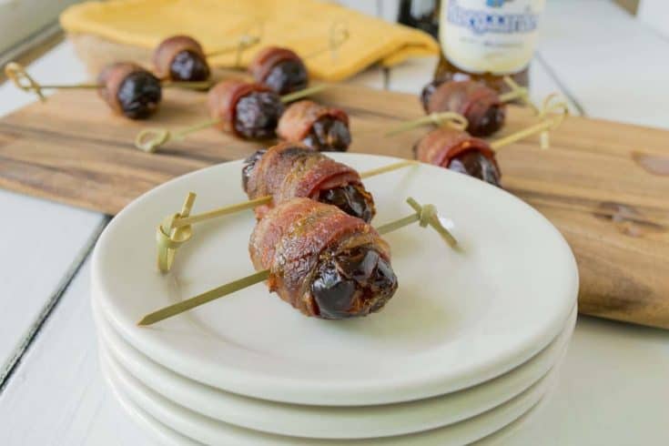 Apple stuffed bacon wrapped dates on white plates with more in background
