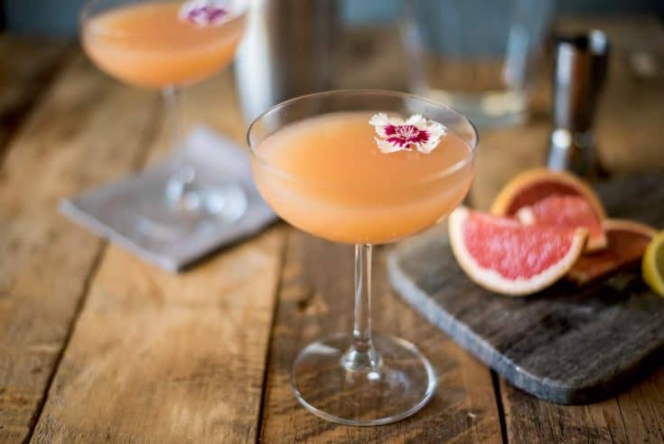 A coupe champagne glass of April Showers cocktail with a flower and grapefruit wedges