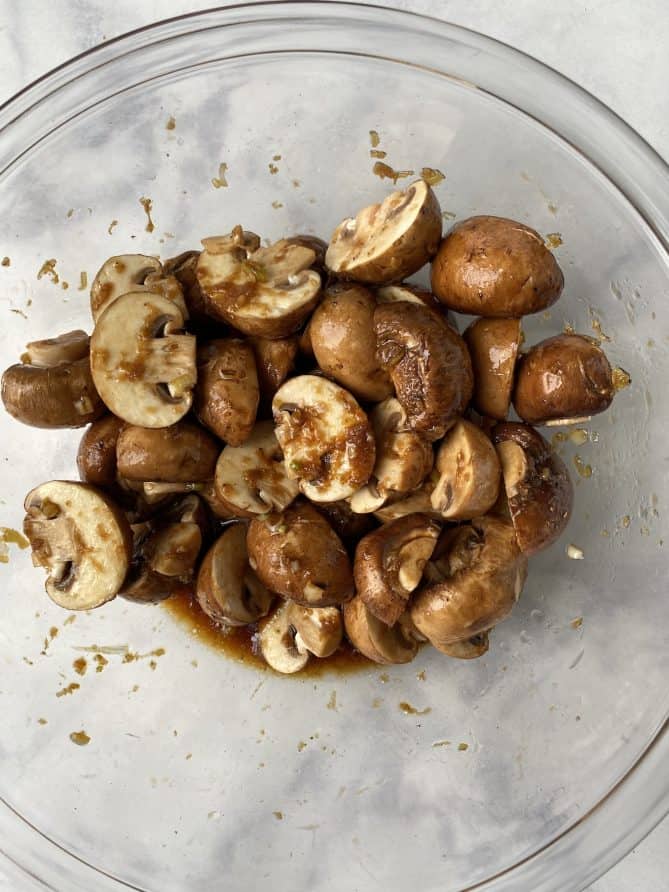 A bowl of mushroom halves marinating in a sauce in a glass bowl