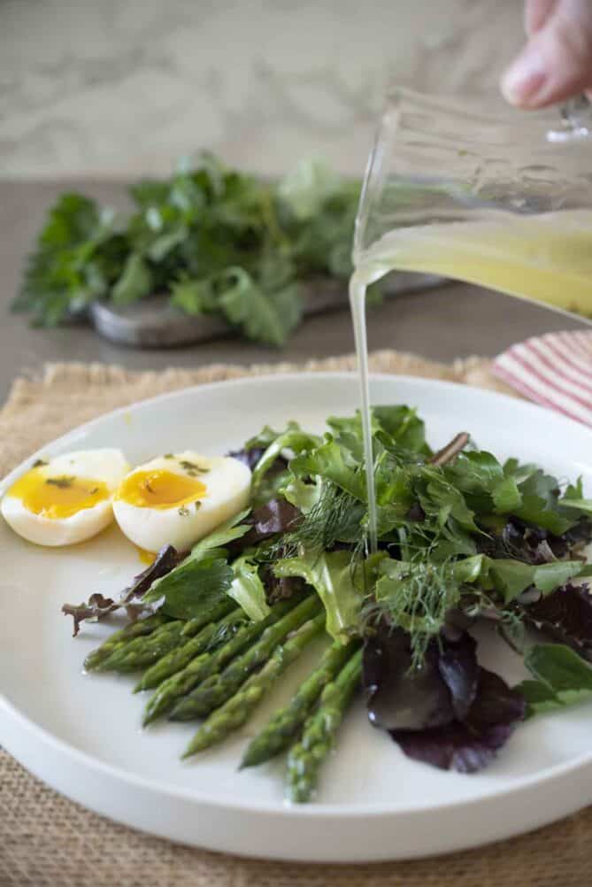 Pouring mint, lemon vinaigrette over a salad on a white plate