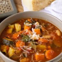 Orange and green vegetables in minestrone soup with grated Parmesan cheese