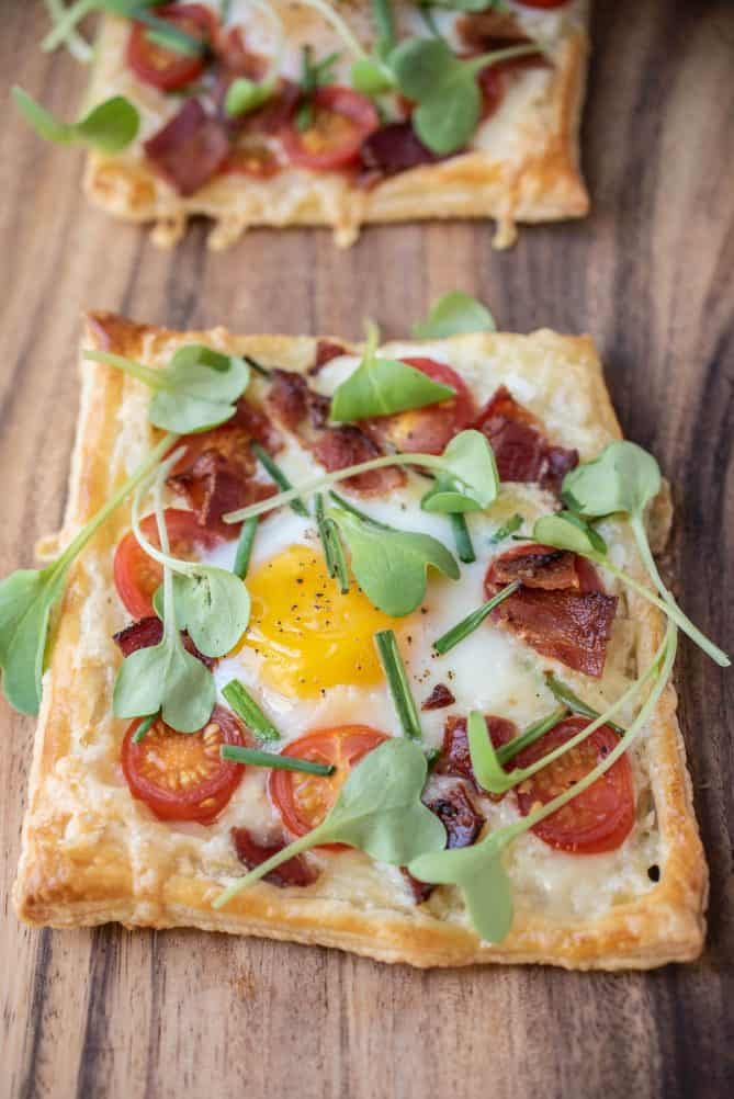 A breakfast tart up close showing the yellow egg and sweet cherry tomatoes
