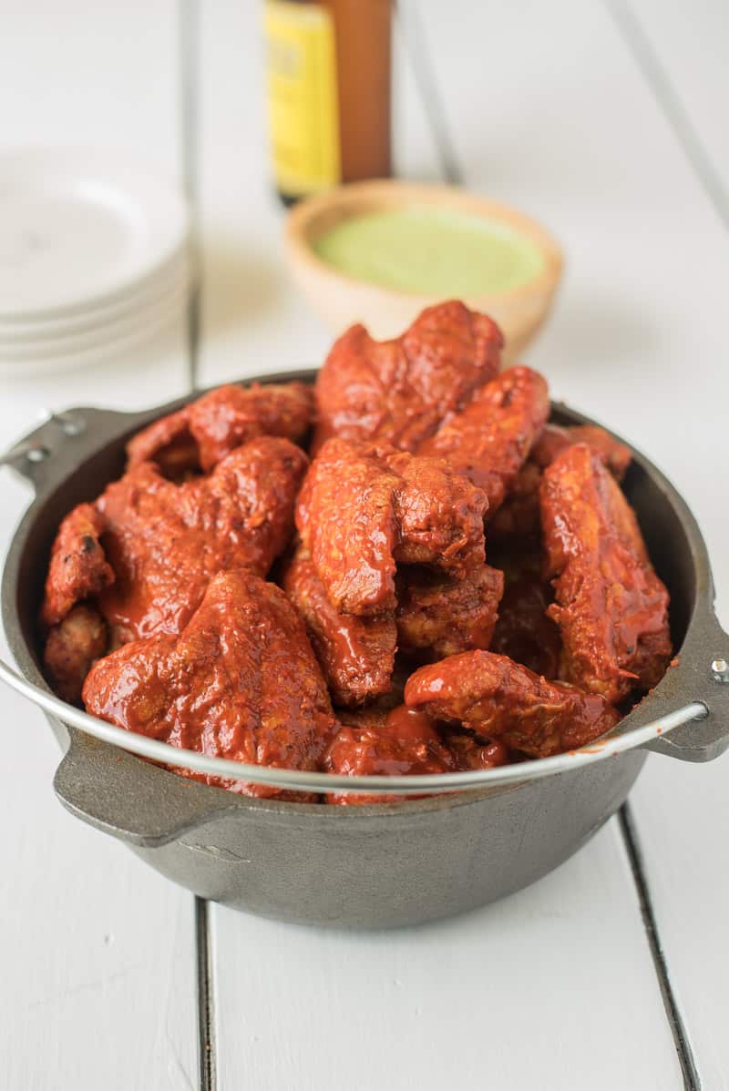 A cast iron pan full of adobo chicken wings with avocado cream for dipping