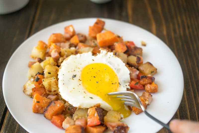 Breakfast potatoes with a fork breaking the yolk of an egg served on a white plate