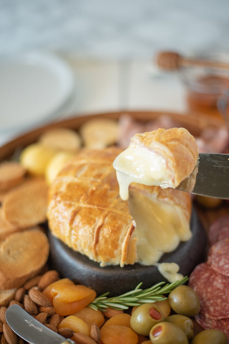A cheesy, melted slice of Baked brie and Black Forest ham in puff pastry on a knife