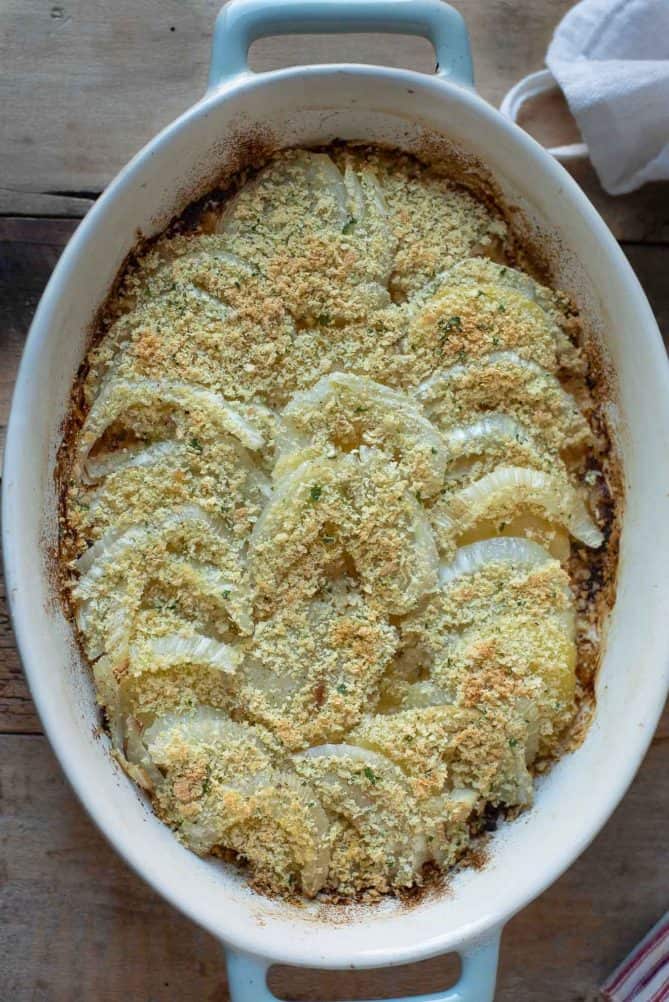 An oval casserole dish with slices of fennel and apple baked with breadcrumbs and parsley