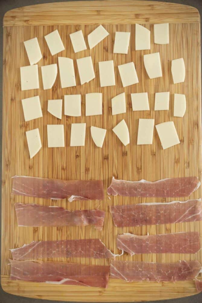 Slices of provolone cheese and prosciutto on a cutting board