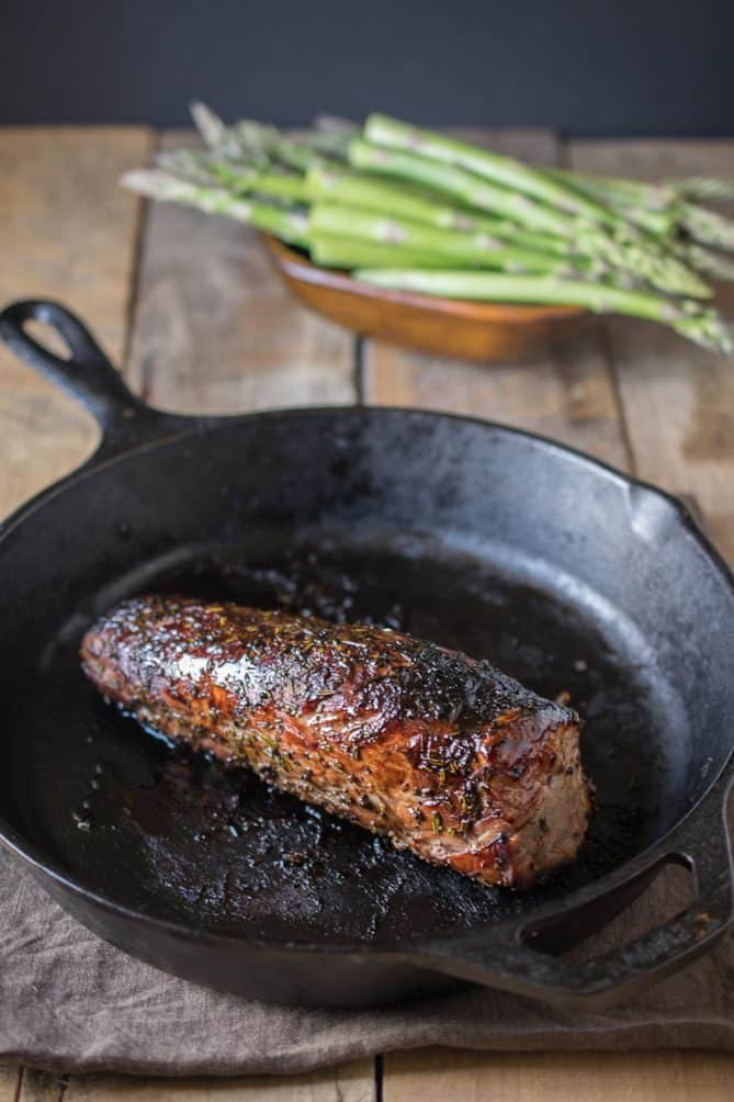 A whole pork tenderloin coated with sweet balsamic glaze in a cast iron skillet