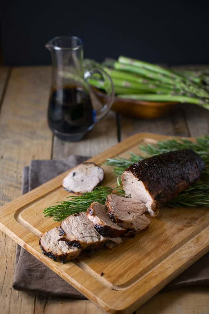 A pork tenderloin on a cutting board, sliced with sprigs of fresh rosemary