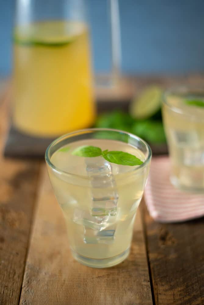 A glass of basil ginger lime tea with ice cubes and basil leaves