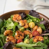 Blackened shrimp nestled on a bed of lettuce with cherry tomatoes and avocado