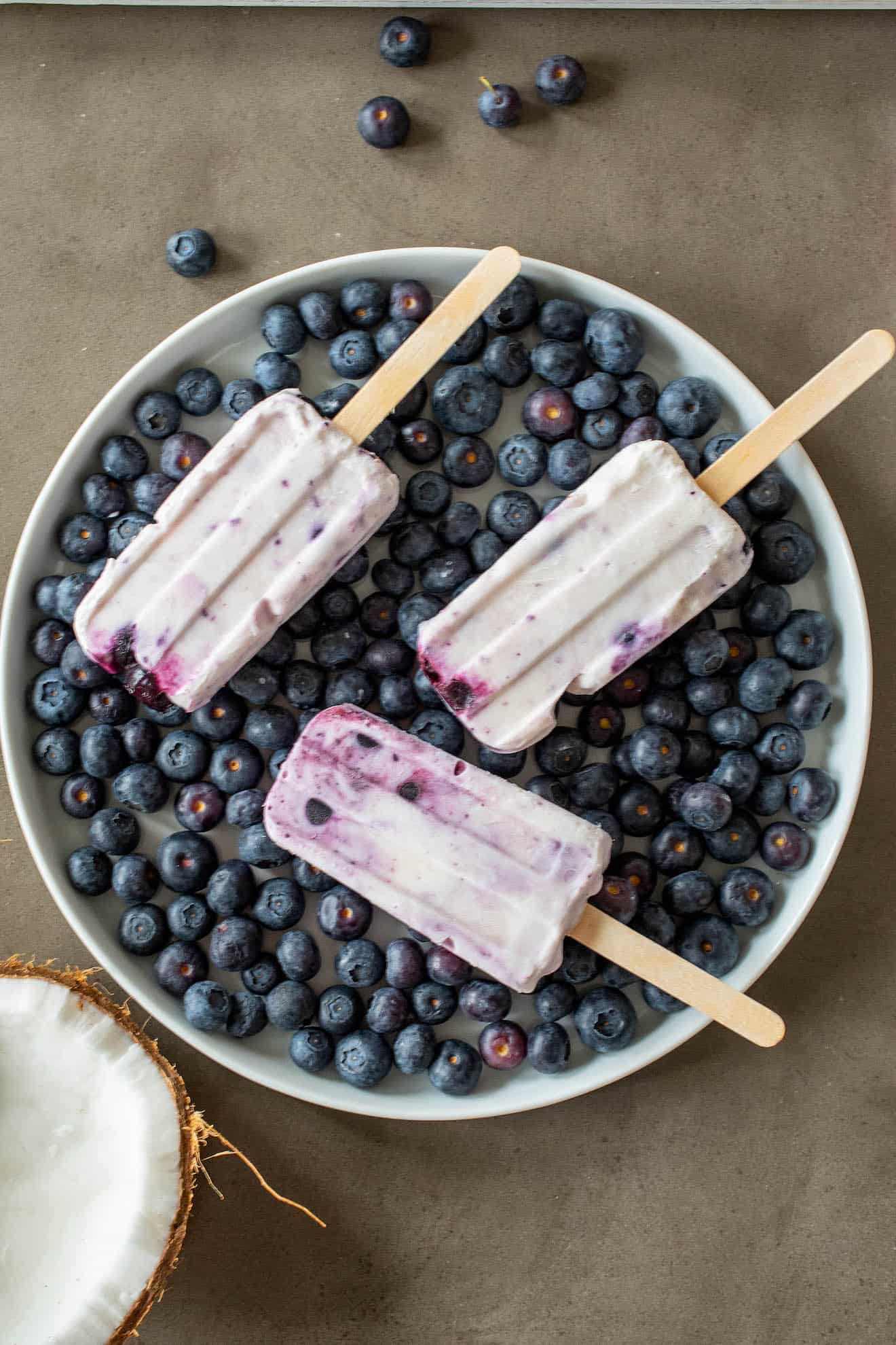 3 popsicles lying down on top of a plate of blueberries