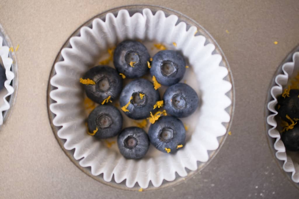 Fresh blueberries and orange zest in the bottom of a muffin cup