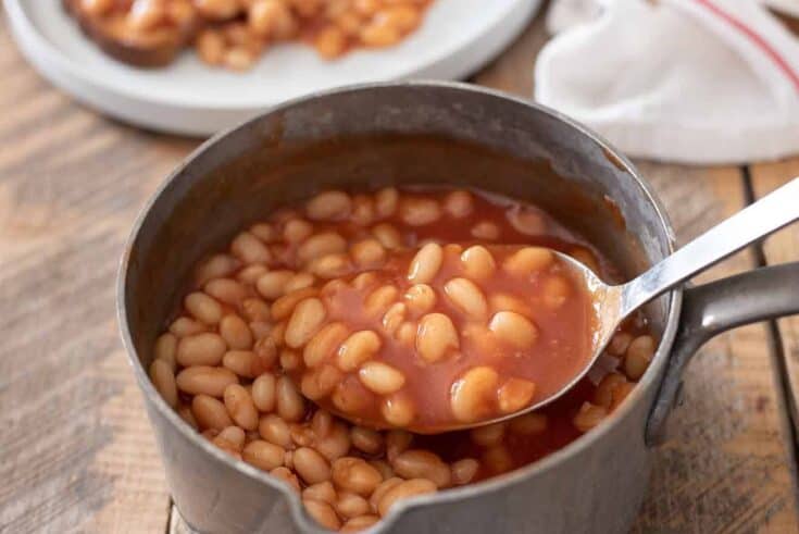 Using a ladle to lift some baked beans from a pan