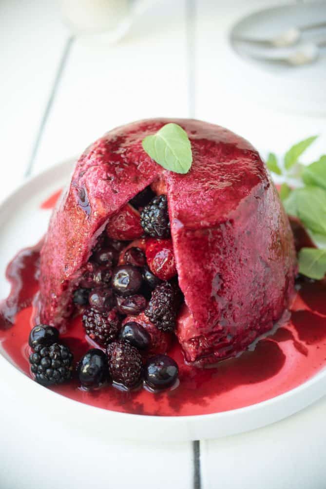 Summer pudding made with bread, cut open with berry fruits pouring out onto a plate