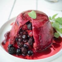 Mixed berries inside a bread pudding covered in colorful berry juice garnished with mint leaves