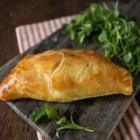 A single cheese and onion pasty on a board with greens