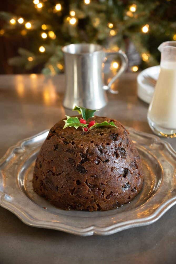 A dark brown Christmas pudding on a plate with brandy sauce