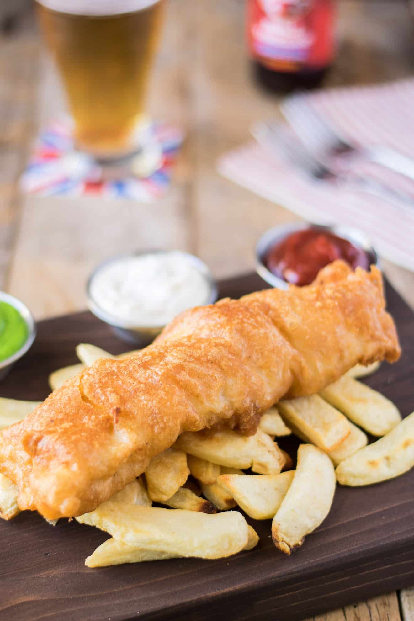 A large piece of fried cod laying on top of chips/French fries