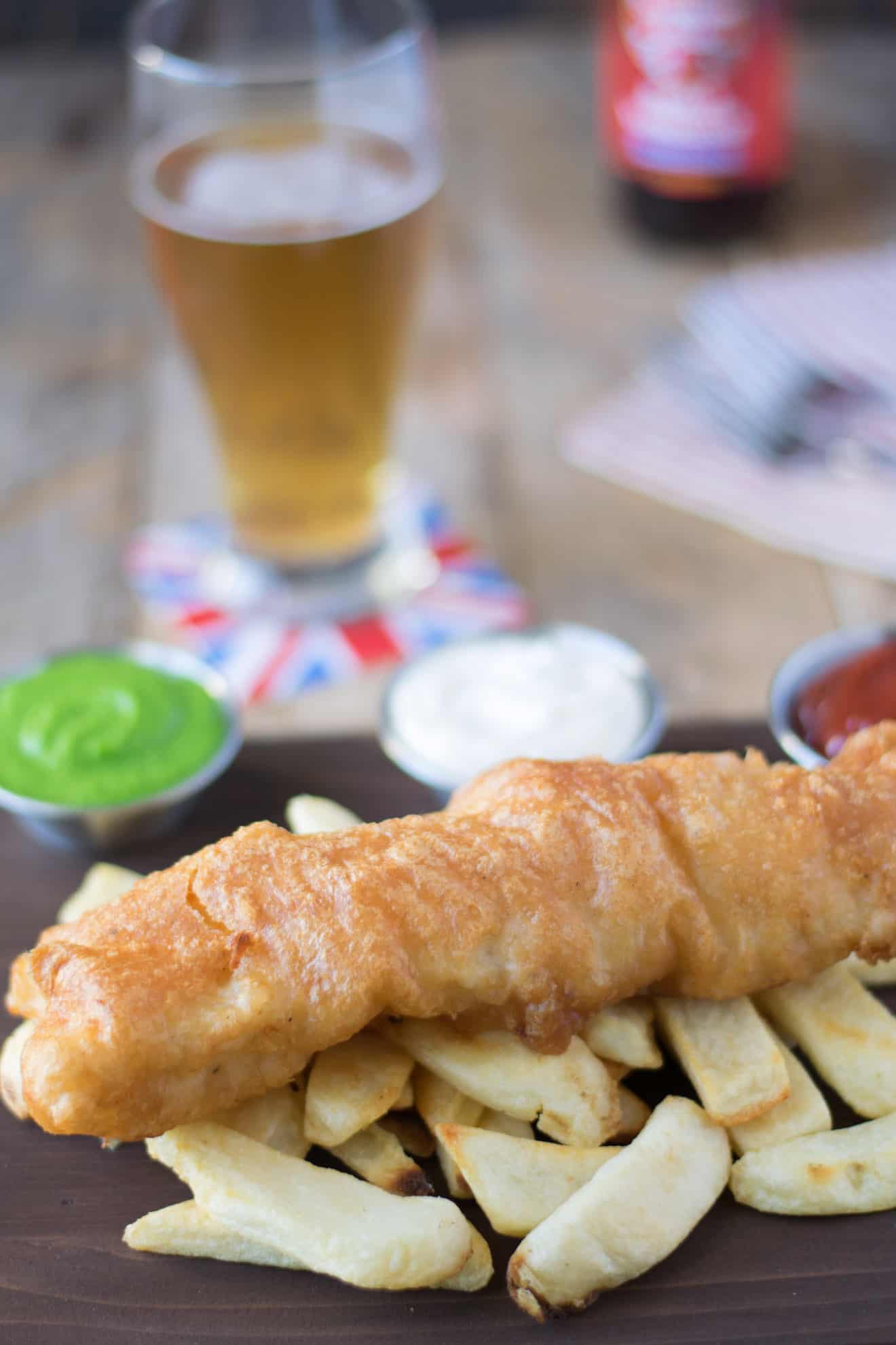 British fish and chips served on a board with a beer and condiments