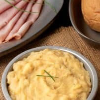 A grey bowl of British pease pudding with ham and a bun