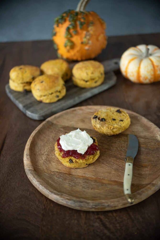 A cut open scone on a wooden round plate with real pumpkins