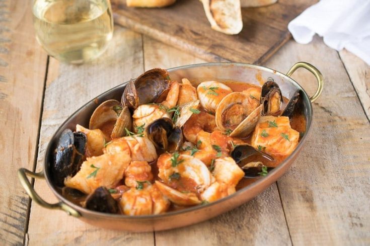 An oval baking dish filled with seafood and shellfish in a tomato broth