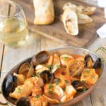 Fish and shellfish in an oval serving dish with a glass of wine and crusty bread