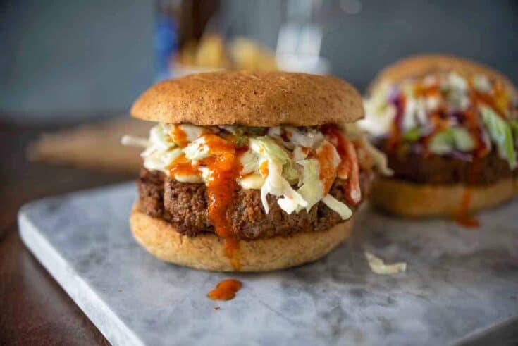 A beef burger in a bun with coleslaw and buffalo sauce