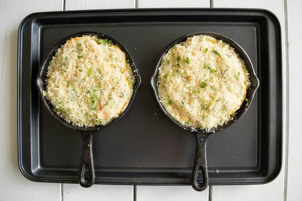 2 mini cast iron skillets with butternut squash and sage gratin on a baking sheet ready for the oven