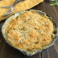 A cast iron skillet of butternut squash and sage gratin with serving spoons