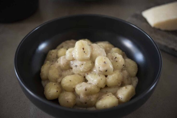 A black bowl filled with potato gnocchi in a cacio e pepe sauce