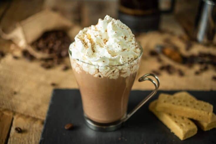 A cafe mochachino in a glass mug topped with whipped cream