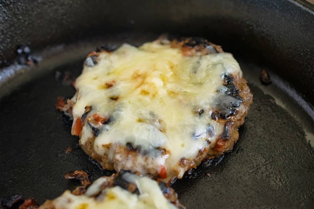 A burger cooking covered in melted cheese