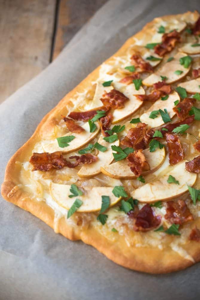 A closeup of the crispy brown edges of flatbread topped with melted fontina, caramelized onions apple slices and crispy bacon.