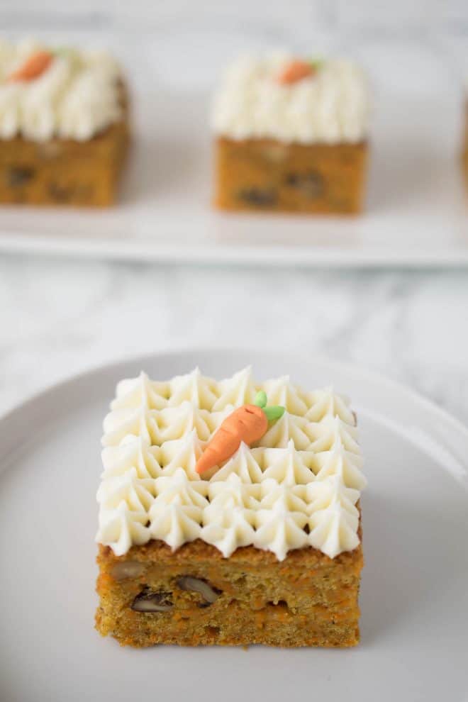 A slice of carrot cake square with decorative frosting on a white plate