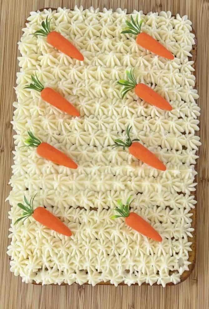 A carrot sheet cake piped with frosting and decorative mini carrots.