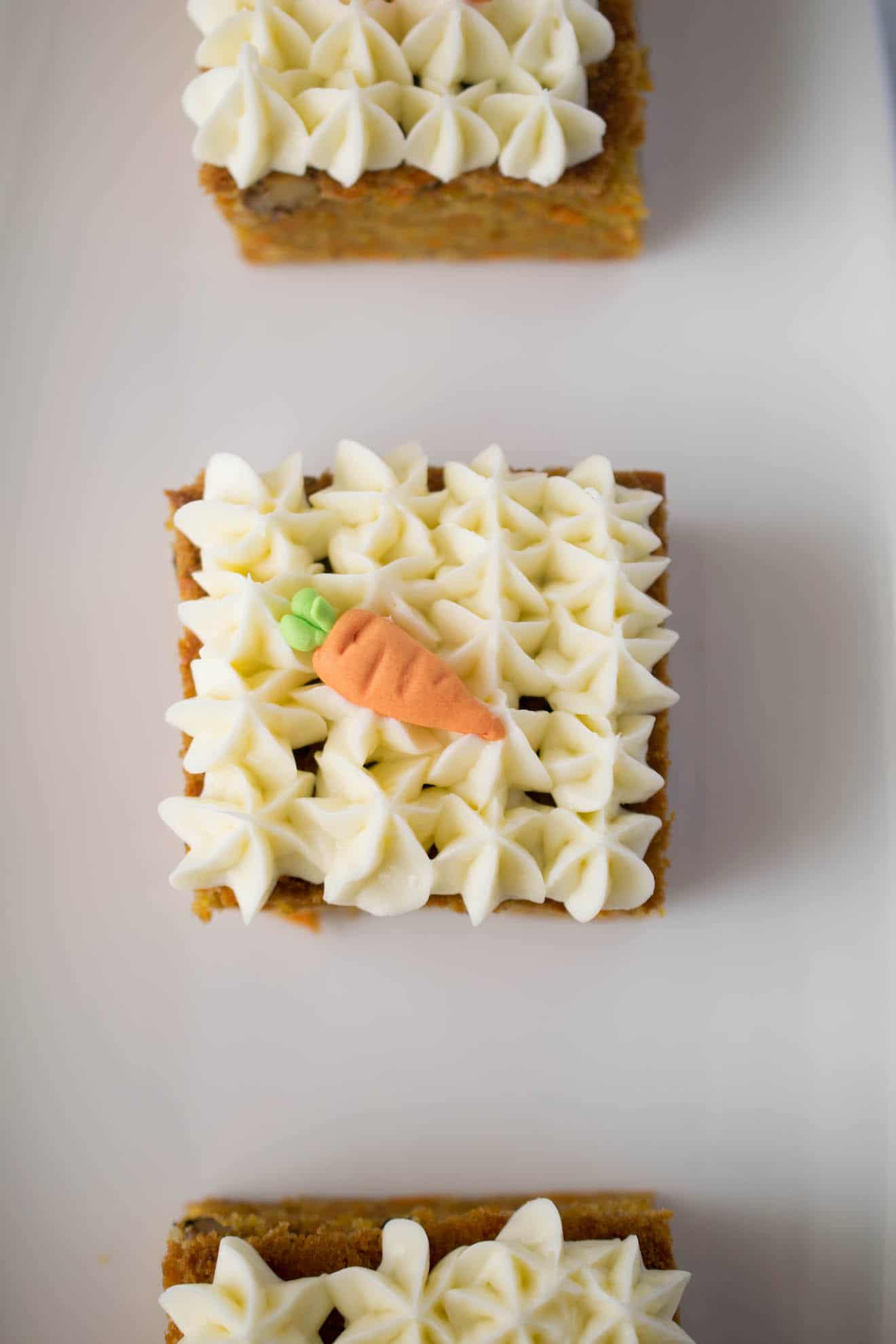 Pretty piped cream cheese frosting on top of carrot cake with a decorative sugar carrot