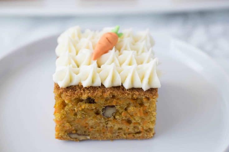 A square of carrot cake topped with cream cheese frosting and a decorative carrot