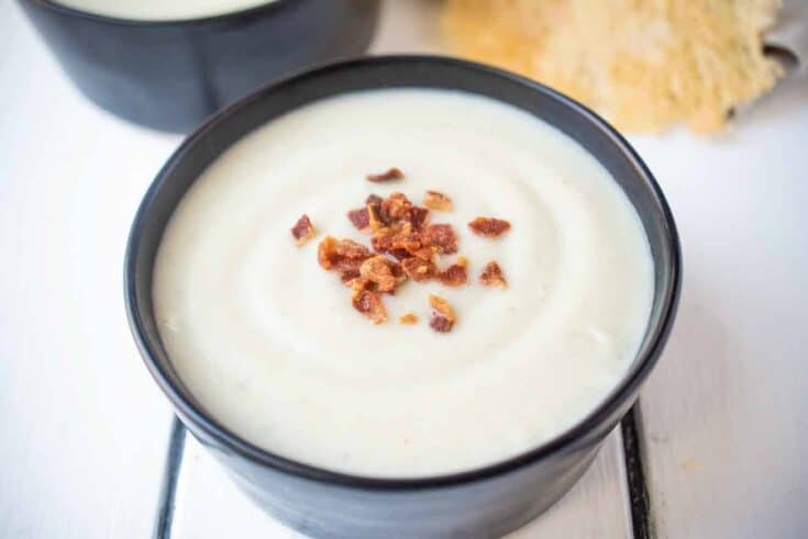 Creamy yet dairy free cauliflower and fennel soup in a black bowl topped with bacon crumbles