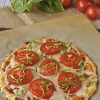Slices of tomato and shredded basil on a cauliflower crust pizza