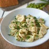A white bowl with cheese tortellini with green peas