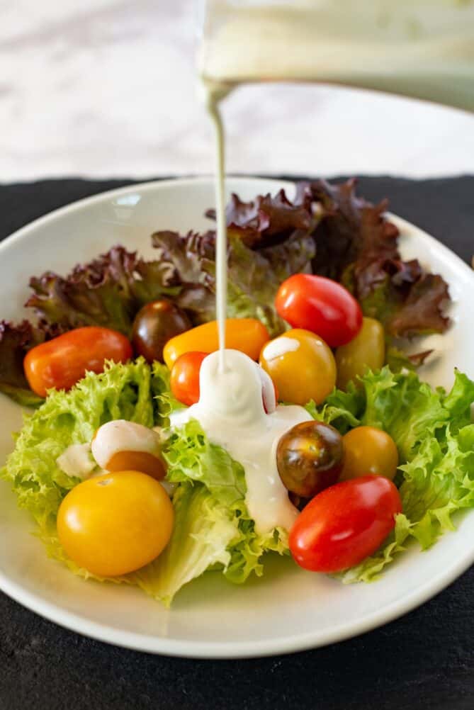 Drizzling salad dressing onto lettuce and cherry tomatoes