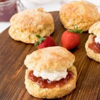 4 English Scones on a board with one sandwiched with jam and clotted cream